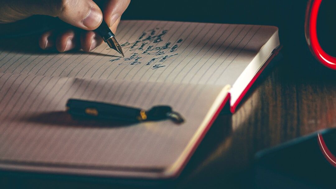 Manos escribiendo en un cuaderno antiguo junto a una lámpara de escritorio